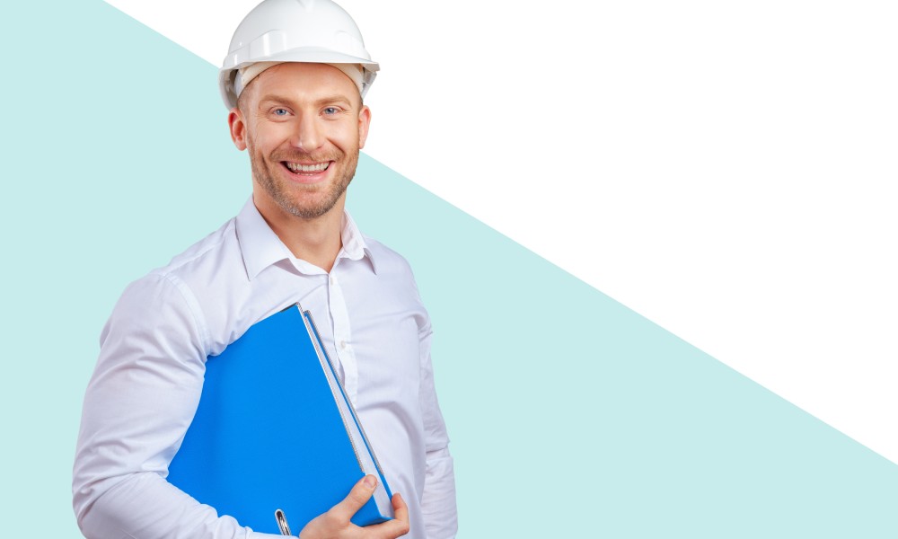 A happy young safety technician is wearing a white shirt, white hard hat, and holding a large blue binder.