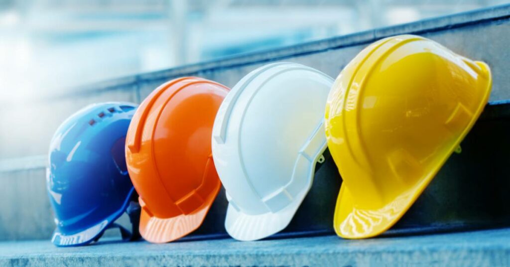 A line of hard hats appears against a blue background. The colors of these hats are blue, yellow, white, and orange.