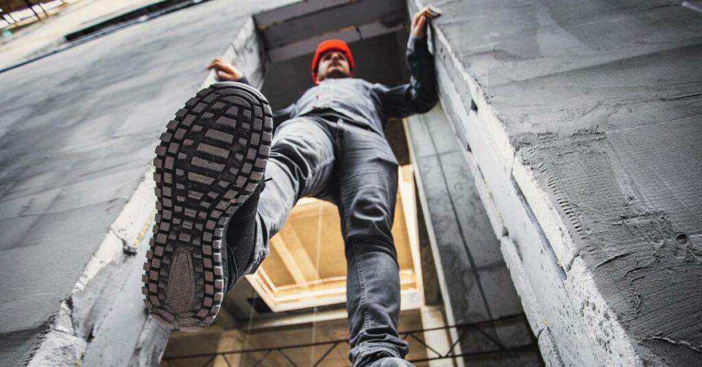 A worker at a construction site stepping through an opening as he holds onto the sides of the building.